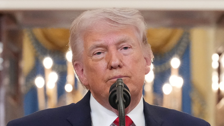 Donald Trump standing in front of a microphone at a podium in a black suit with a red tie