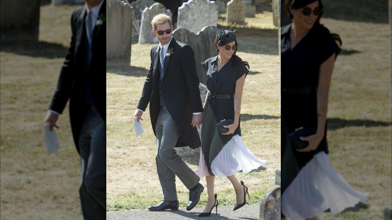 Prince Harry and Meghan Markle holding hands and wearing sunglasses while walking through a graveyard.