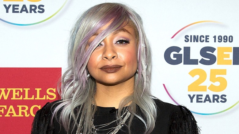 Sporting a purple and silver hairdo and a black outfit, Raven-Symoné gives the camera an intense stare.