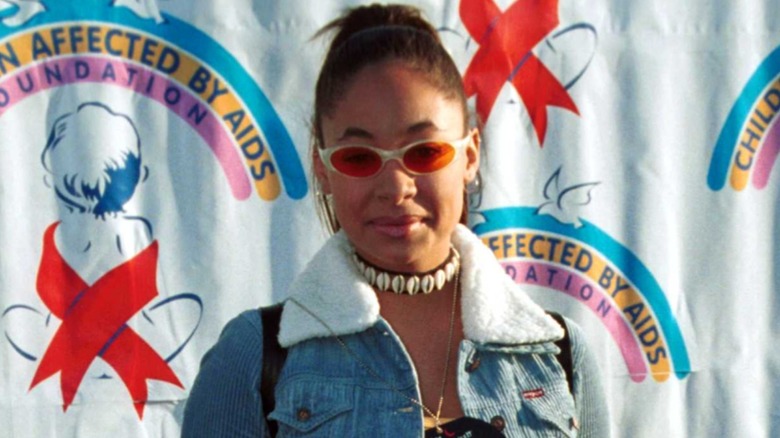 Sporting a denim jacket and beaded necklace, Raven-Symoné looks at the camera through orange sunglasses.