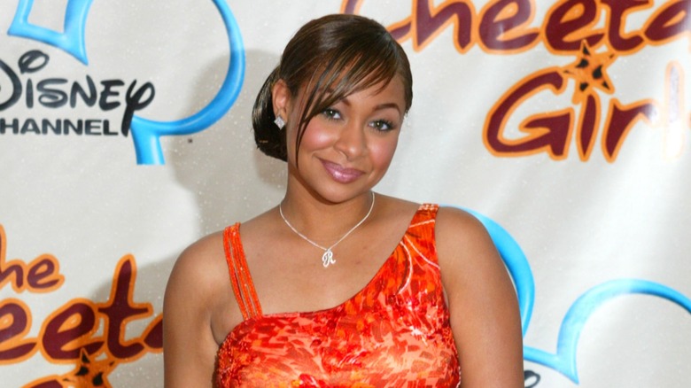 Wearing an orange dress and relaxed hair, Raven-Symoné sports a soft smile.