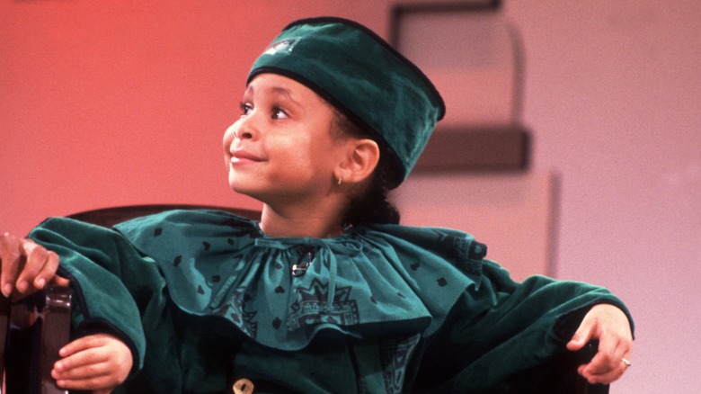 Wearing a dark teal attire, Raven-Symoné gleefully stares upward while facing sideways.