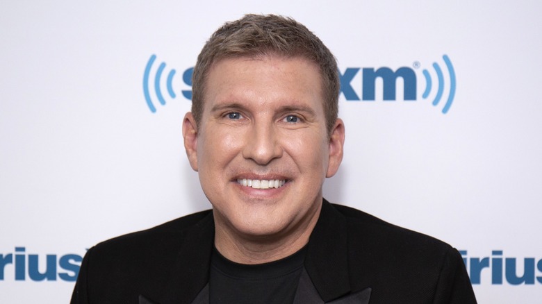 Wearing an all-black suit and shirt combo, Todd Chrisley smiles as he looks directly at the camera.