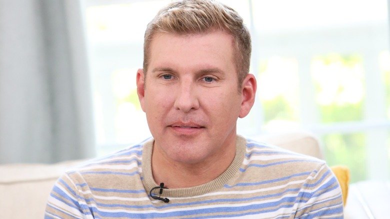 Todd Chrisley, who is wearing a microphone and dressed in a stripped shirt, gazes away from the camera.