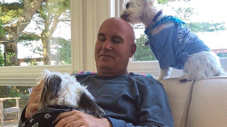Dennis Shields relaxing on a couch with his two small white dogs