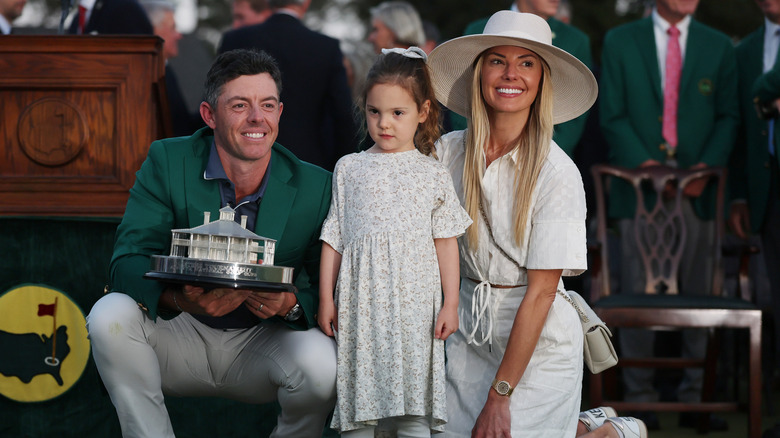 Rory McIlroy and Erica Stoll smiling for photos with their child