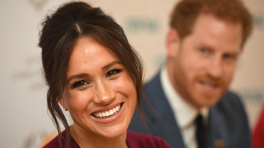 Meghan Markle smiling with Prince Harry in the background