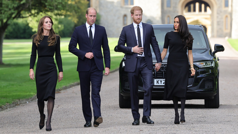 Kate Middleton, Prince William, Prince Harry, and Meghan Markle walk together outside wearing black.