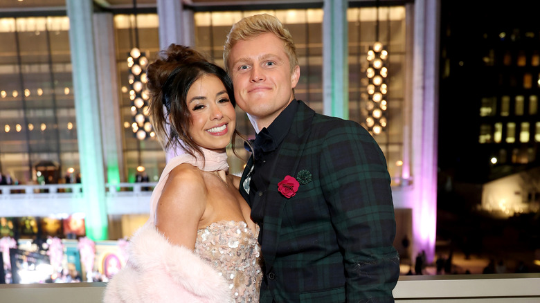 Jen Affleck in a pink dress and Zac Affleck in a plaid suit posing for the camera