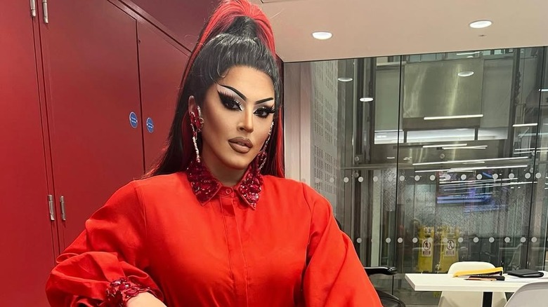 Drag queen Cherry Valentine sitting in a chair wearing a red long sleeved dress