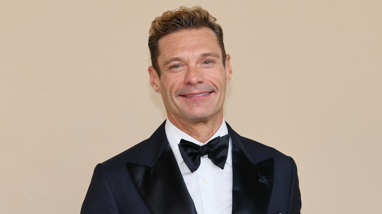 Close-up photo of Ryan Seacrest smiling in a black and white suit in April 2026.