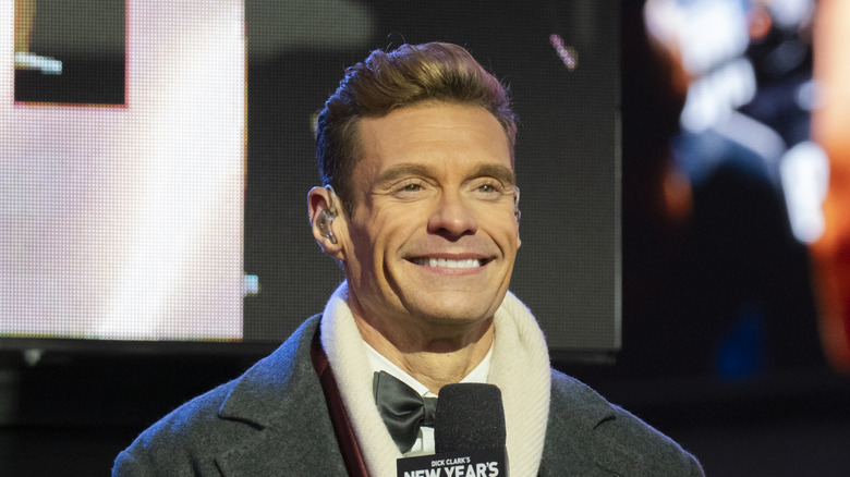 Ryan Seacrest smiling while holding a mic on New Year's Eve