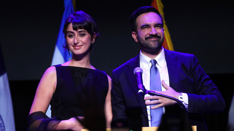 Zohran Mamdani and his wife, Rama Duwaji, smiling on a stage