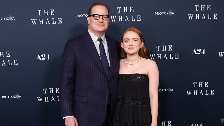Brendan Fraser and Sadie Sink pose in front of a backdrop advertising The Whale