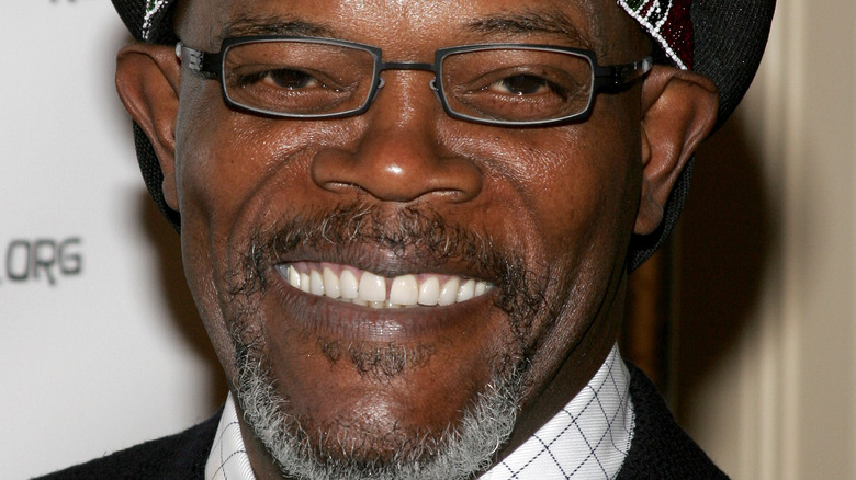 Samuel L. Jackson smiles while wearing glasses and a beaded hat