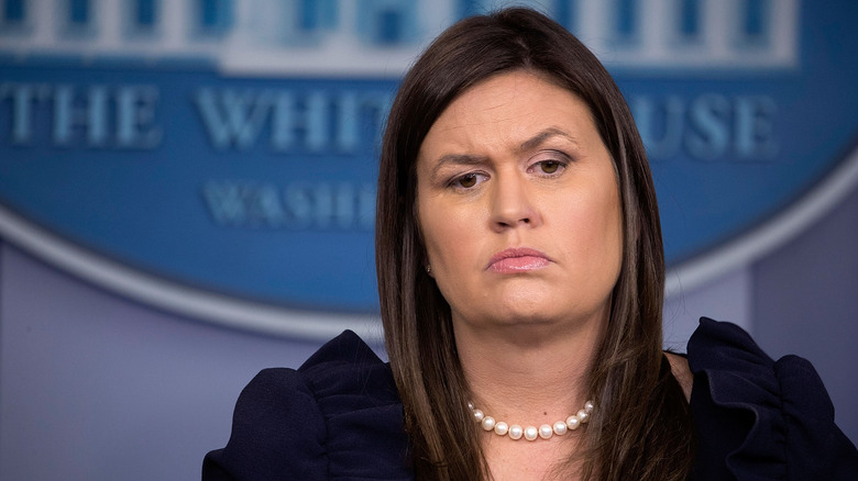 Sarah Huckabee Sanders frowning in a black dress and pearls