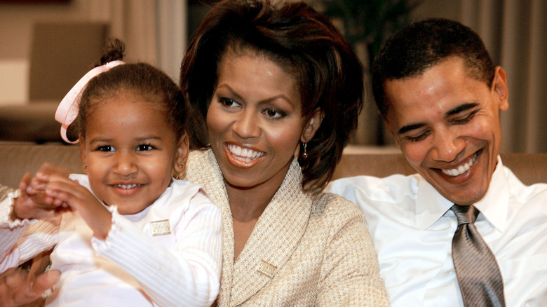 Sasha Obama posing for cameras with parents Michelle and Barack Obama.