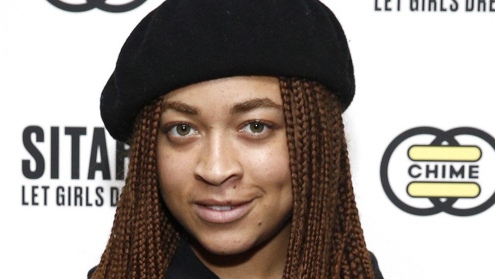 Satchel Lee, smiling, wearing a beret, braids, red carpet