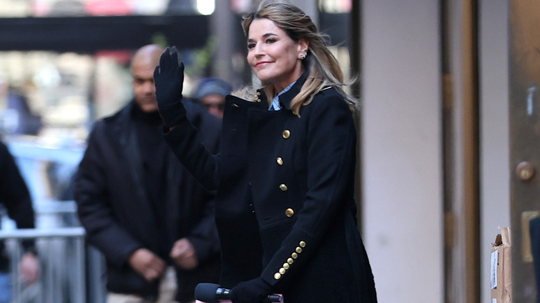 Savannah Guthrie waves to fans in New York City in a black coat with gold buttons