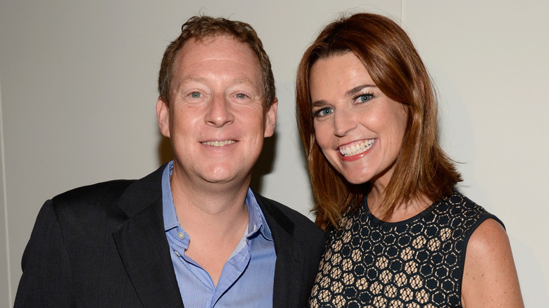 Michael Guthrie in a black jacket and blue striped shirt with Savannah Guthrie in a black sleeveless dress