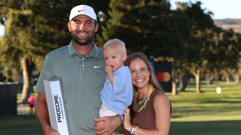 Scottie Scheffler, his son, and his wife posing on a golf course.