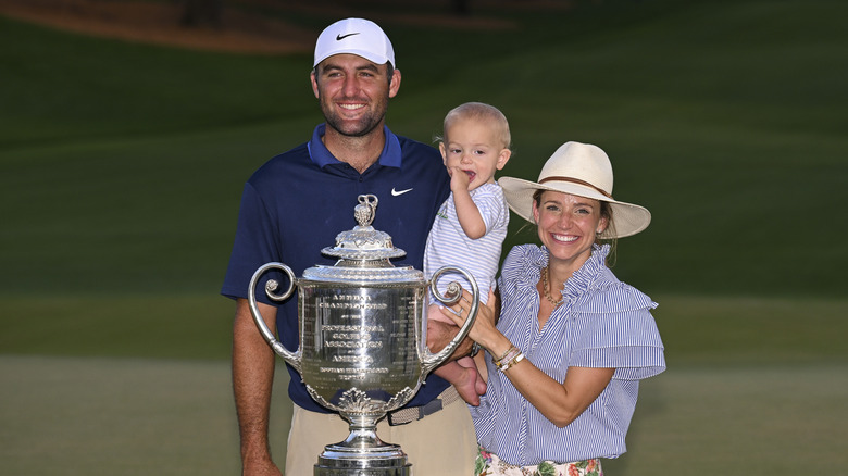 Scottie Sheffler and his family posing on a golf course with a large trophy.
