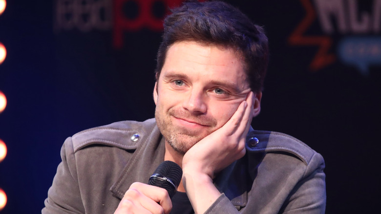 Sebastian Stan smiling while holding microphone