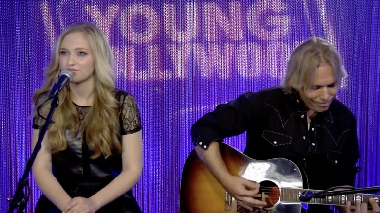 A teenage Maggie singing alongside a guitar