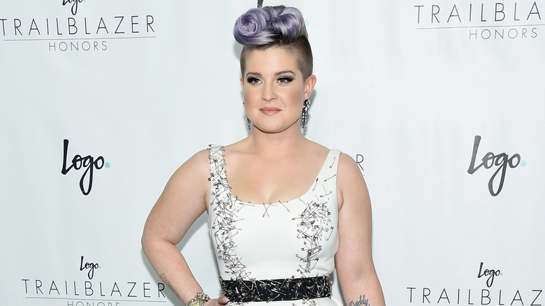 Kelly Osbourne with a purple pompadour wearing a black belted floral dress