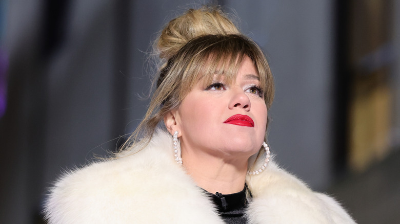 Kelly Clarkson with serious expression while wearing faux white fur and red lipstick