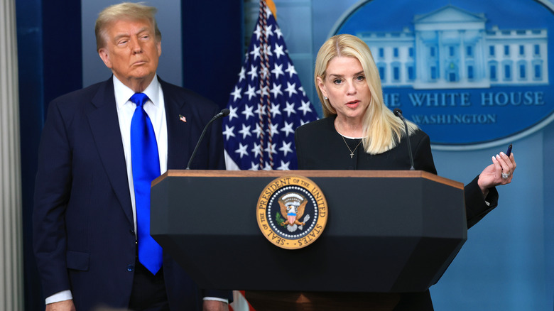 Pam Bondi behind the podium next to Donald Trump