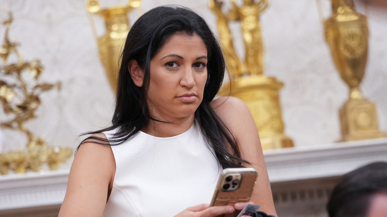 Katie Miller looking disgruntled while holding a phone and wearing a white strapless shirt