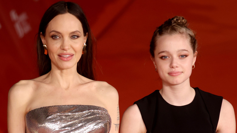 Angelina Jolie smiling with her hair down beside a smiling Shiloh Jolie, whose hair is in a braided bun.
