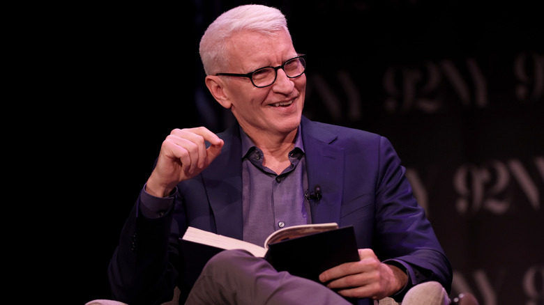 Anderson Cooper laughing on stage with book in lap.
