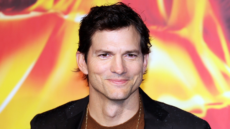 Ashton Kutcher smiling and wearing a gold chain.