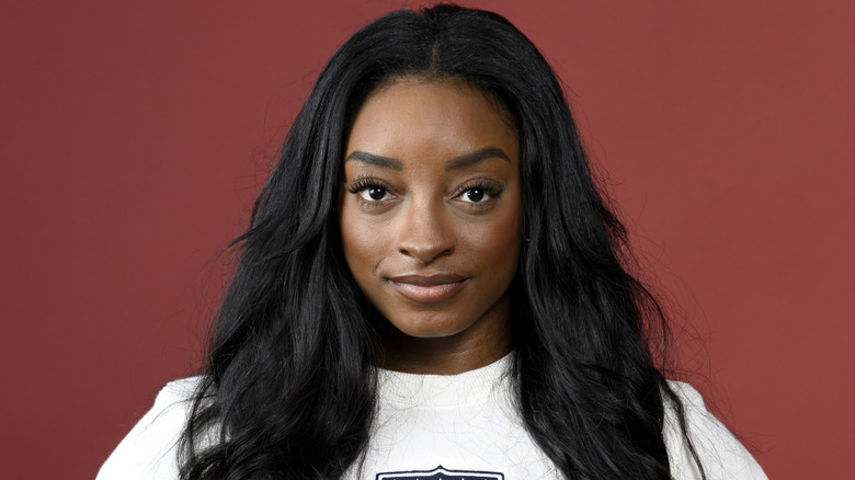Simone Biles poses against a maroon background with her hair down