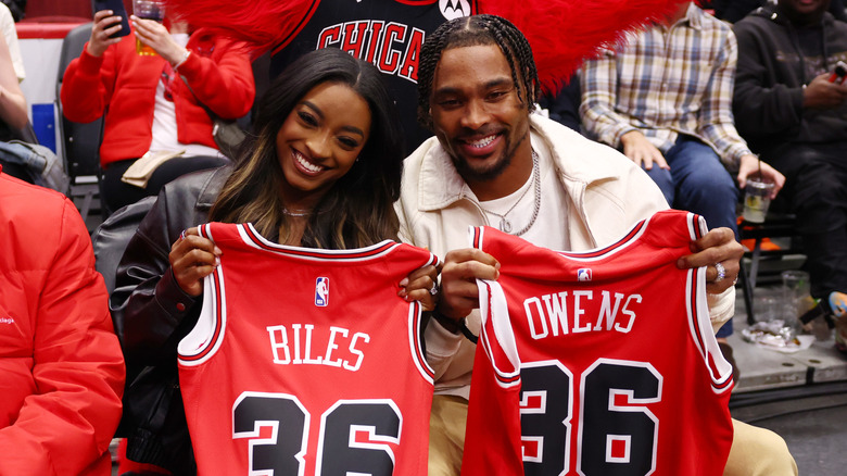 Simone Biles and Jonathan Owens hold up basketball jerseys with their names