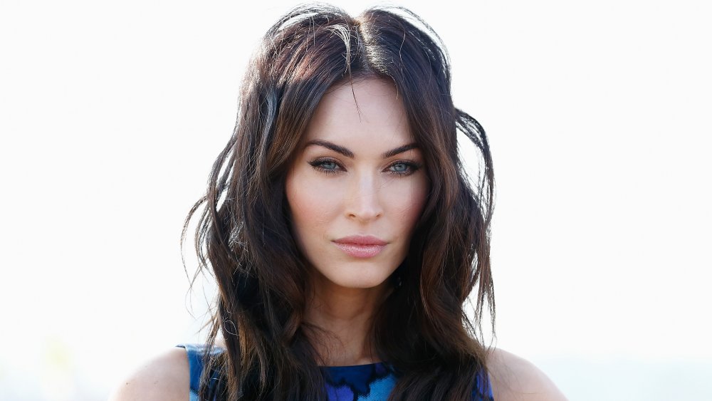 Megan Fox in a blue dress, looking out with a serious expression