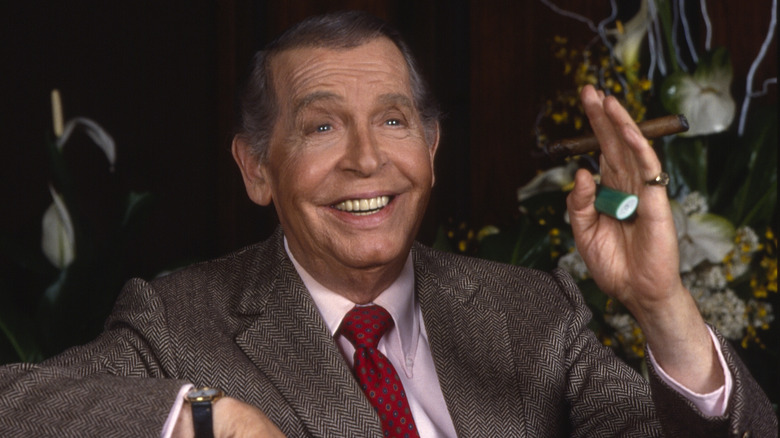 Milton Berle wearing a grey suit and red tie