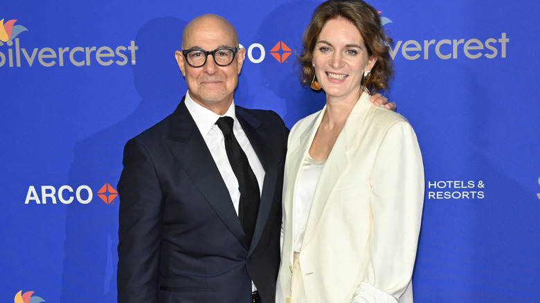 Stanley Tucci and Felicity Blunt wearing suits.