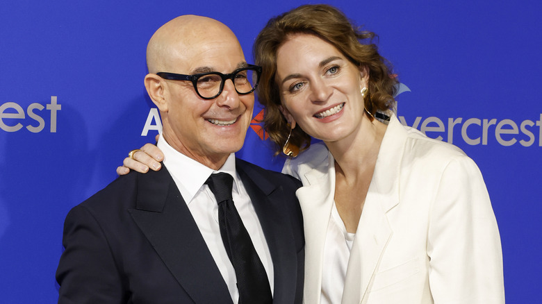Stanley Tucci and Felicity Blunt smiling while posing playfully on the red carpet