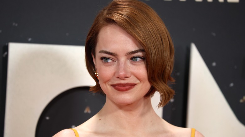 Emma Stone with a red bob smirking on the red carpet