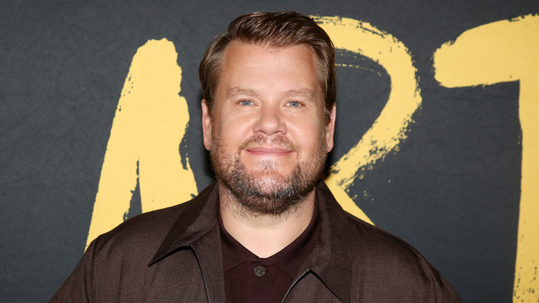 James Corden wearing a brown jacket and maroon button up shirt