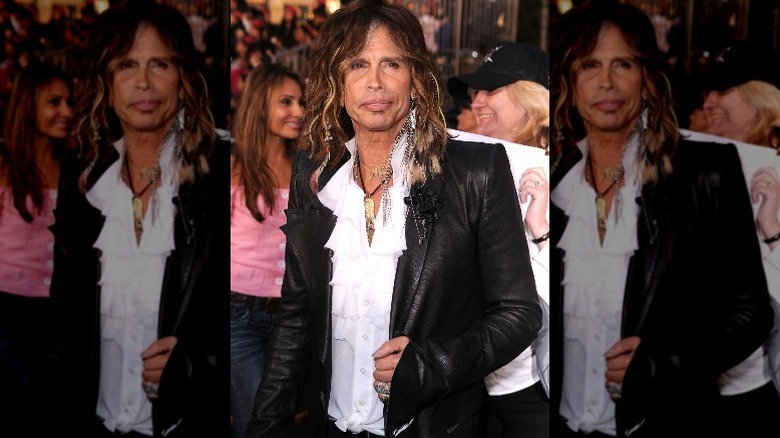 Steven Tyler posing in a leather blazer and white frilly shirt