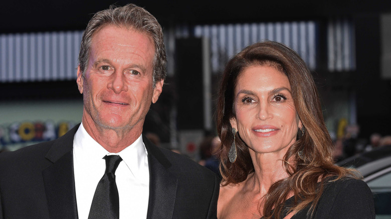 Rande Gerber wearing a black suit and tie with Cindy Crawford wearing a black cutout one shouldered gown and silver dangling earrings