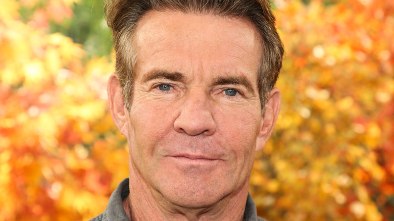 Dennis Quaid posing in front of leaves