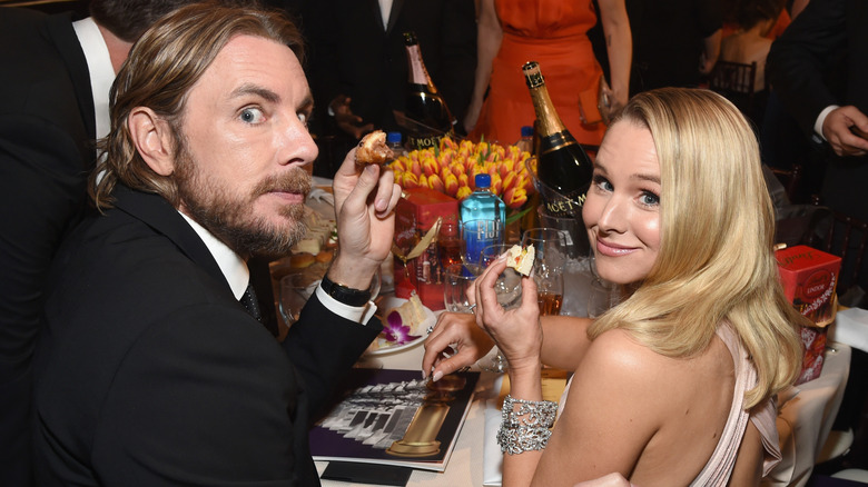 Dax Shepard and Kristen Bell at table with bite-sized food in hands
