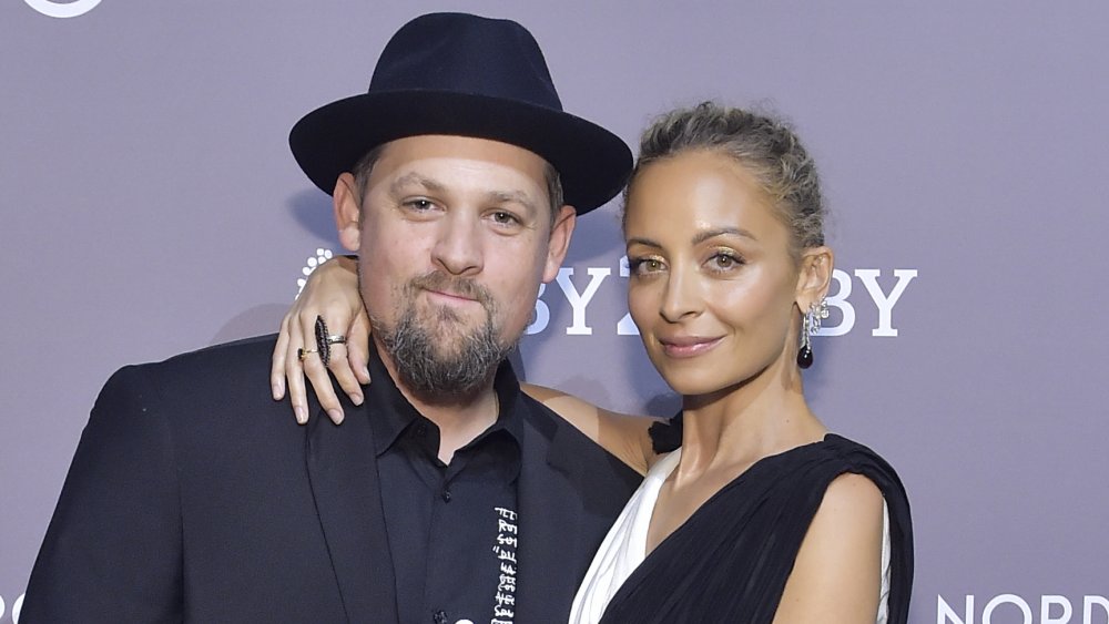 Joel Madden in a black suit and hat, Nicole Richie in a white-and-black dress, posing with their arms around each other and small smiles