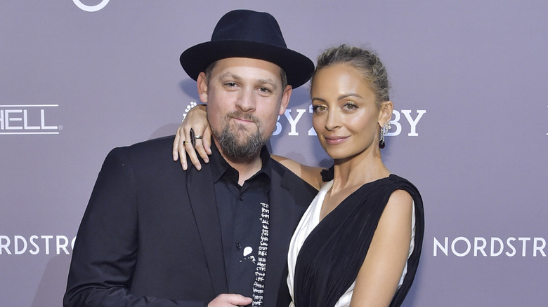 Joel Madden in a black suit and hat, Nicole Richie in a white-and-black dress, posing with their arms around each other and small smiles