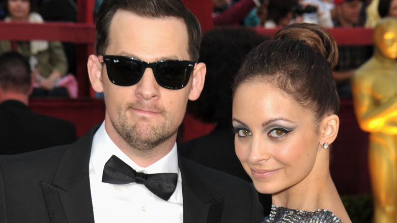 Joel Madden in a black tux and sunglasses, Nicole Richie in a silver dress smirking at the 2010 Oscars